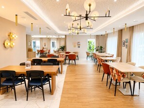 A spacious dining area with multiple tables and chairs, a modern chandelier, and a view of the outdoors through large windows. - Zenao Appart'hôtels Aix Rambot (Aix-en-Provence)