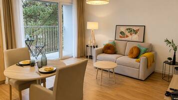 A modern living room with a sofa, a dining table, and a balcony with a view of trees.