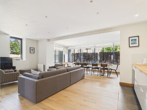 A modern living room with a sectional sofa, a dining area with chairs and a table, and a kitchen area with cabinets. - Superb house for 10, near beach (Dinard)