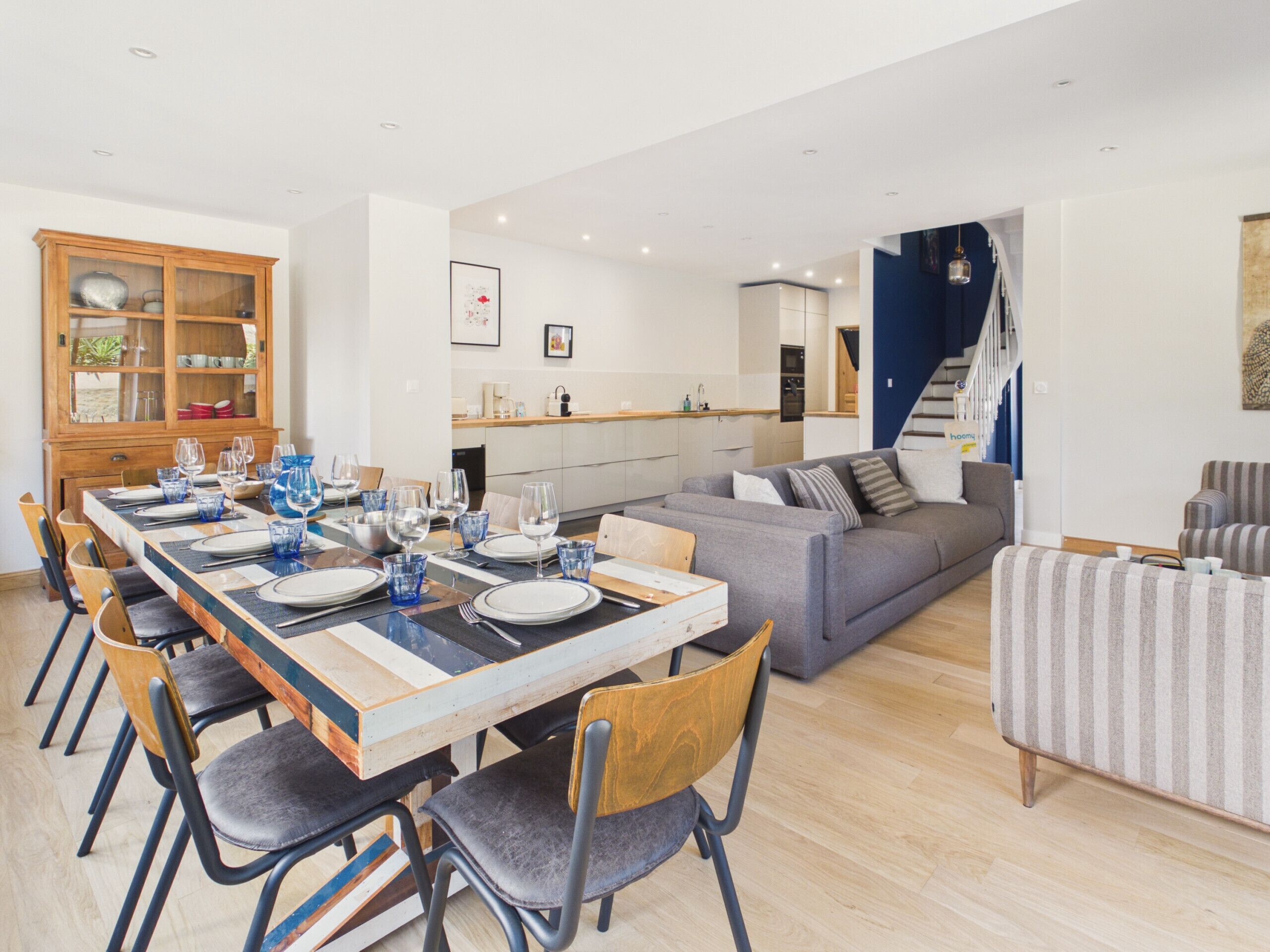 A modern living space with a dining area, kitchen, and a staircase leading to an upper level.
