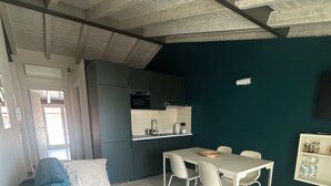 Ein modernes Wohnzimmer mit einem blauen Sofa, einem Esstisch mit Stühlen, einer Küchenzeile mit dunklen Schränken und einer Wand in Türkis.