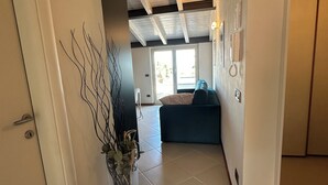 Ein Flur mit einer Tür, einer Vase mit Zweigen, einem blauen Sofa und einem Telefon.