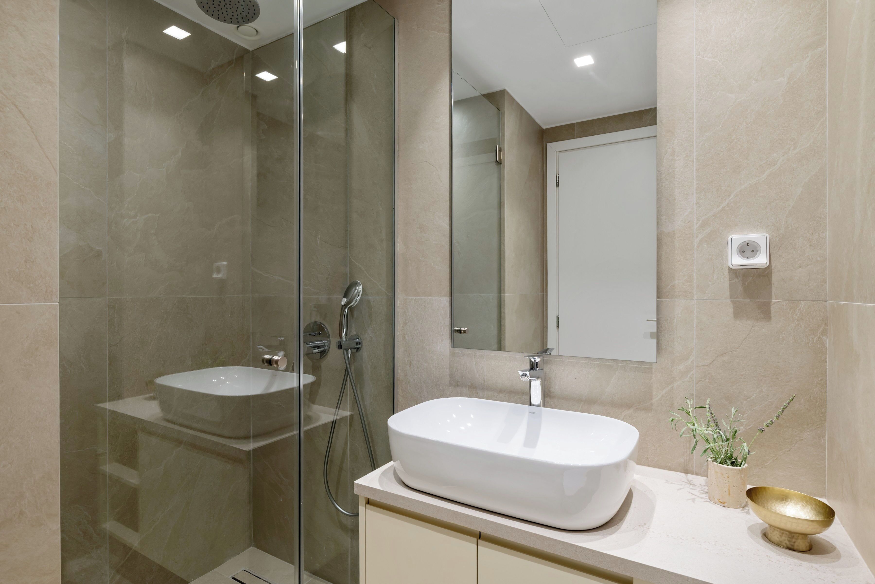 Un baño moderno con ducha envuelta en vidrio, lavamanos independiente y una pequeña planta en maceta.