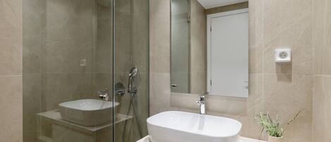 Un baño moderno con ducha envuelta en vidrio, lavamanos independiente y una pequeña planta en maceta.