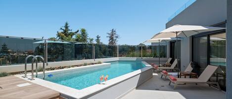 A modern outdoor pool area with a clear blue pool, sun loungers, and a glass-enclosed patio.