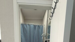 A narrow bathroom with a striped shower curtain, a white toilet, and a white sink with a mirror above it. - Olivento Pansiyon (Ayvalik)
