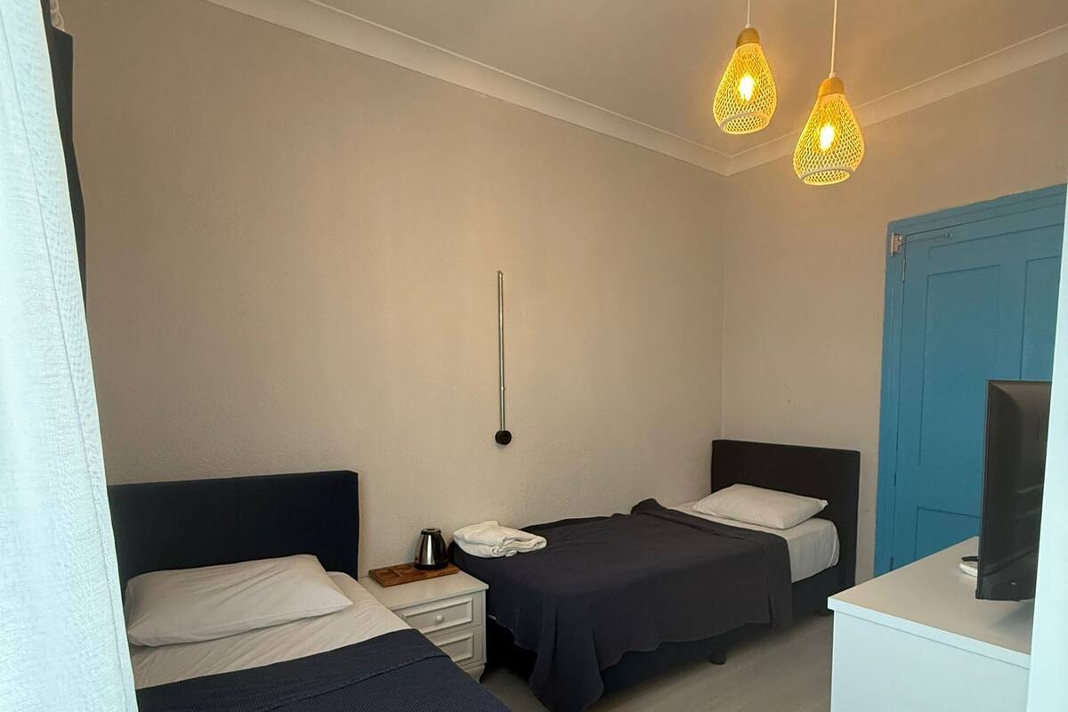 Habitación de hotel con dos camas, un escritorio, un televisor y lámparas colgantes.