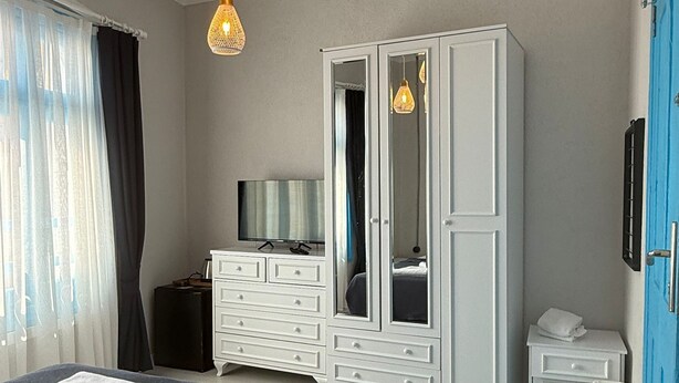 A bedroom with a bed, a dresser, a TV, and a wardrobe. - Olivento Pansiyon (Ayvalik)