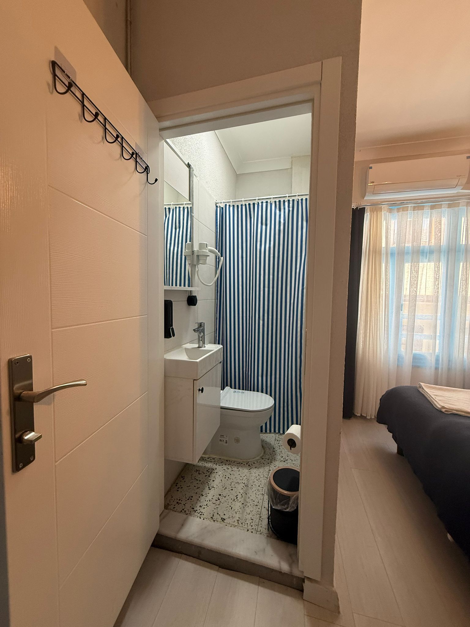 Una habitación de hotel con baño, una cama y un ventanal con cortinas.