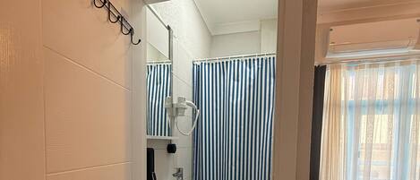 Una habitación de hotel con baño, una cama y un ventanal con cortinas.