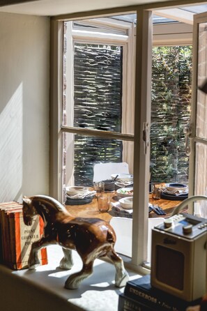 A window with a view of a dining area, a horse figurine, and a vintage radio. - Plum Tree Cottage -  a cottage that sleeps 4 guests  in 2 bedrooms (Sudbourne)