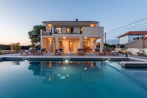 Ein zweistöckiges Haus mit Swimmingpool, Liegestühlen und Essbereich.