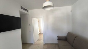 Un salon moderne doté d’un téléviseur à écran plat, d’un canapé, d’une suspension et d’une porte donnant sur une autre pièce.