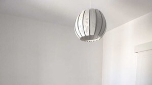 Une chambre avec un lit simple, une tête de lit blanche, deux tables de chevet, un luminaire suspendu et une porte située sur le côté droit.