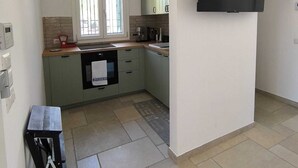 Une cuisine moderne équipée d’un four à micro-ondes encastré, d’une fenêtre avec stores, d’un téléviseur noir fixé au mur et d’une petite table avec une chaise.