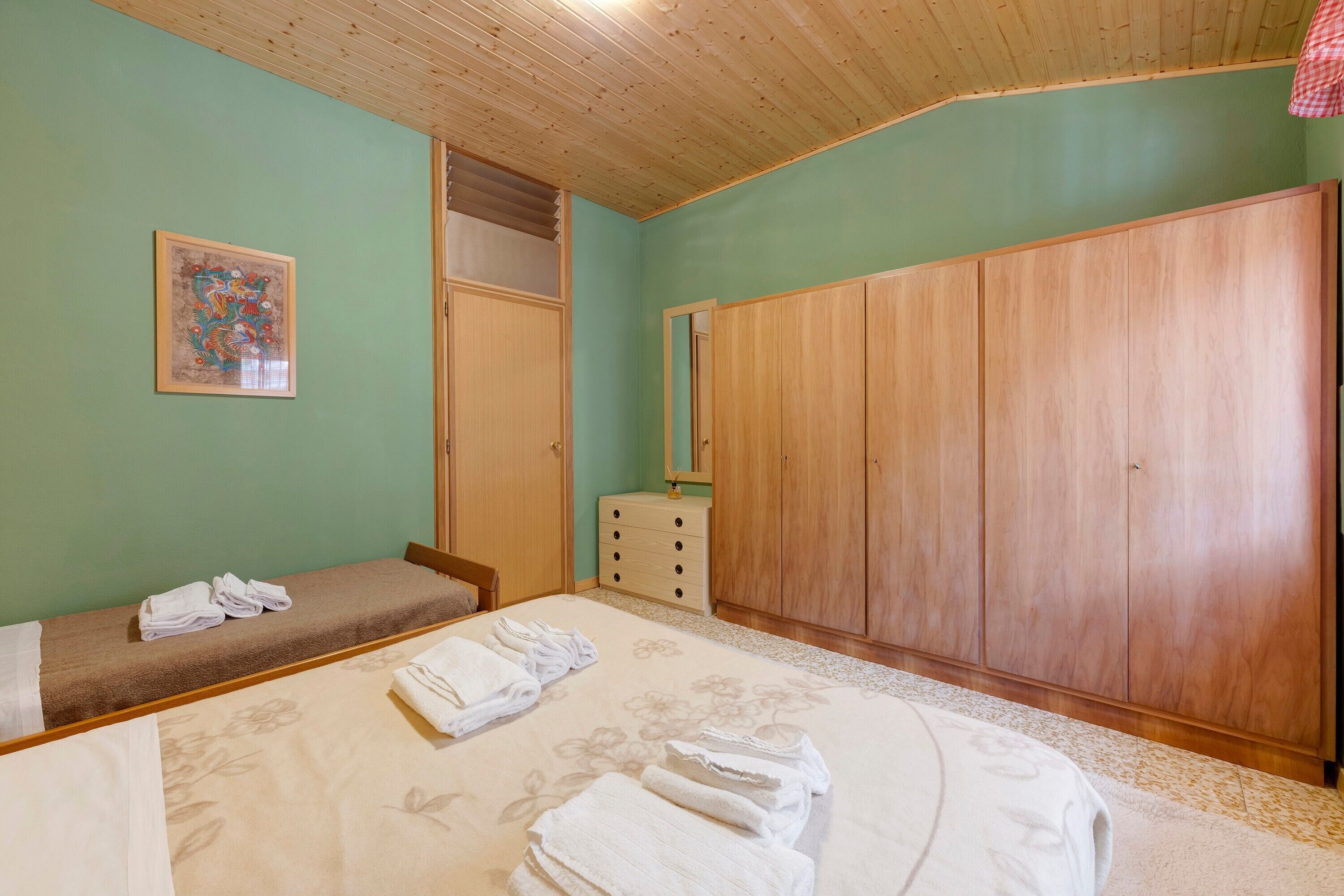 A bedroom with a bed, a bench, a wardrobe, and a dresser.