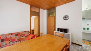 Ein Zimmer mit einem Holztisch, Stühlen, einem gemusterten Sofa, einer kleinen weißen Kommode und einer Wanddekoration.