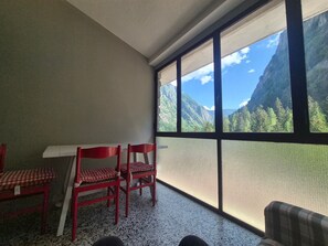Ein Zimmer mit großem Fenster, einem Tisch mit Stühlen und Blick auf eine gebirgige Landschaft.