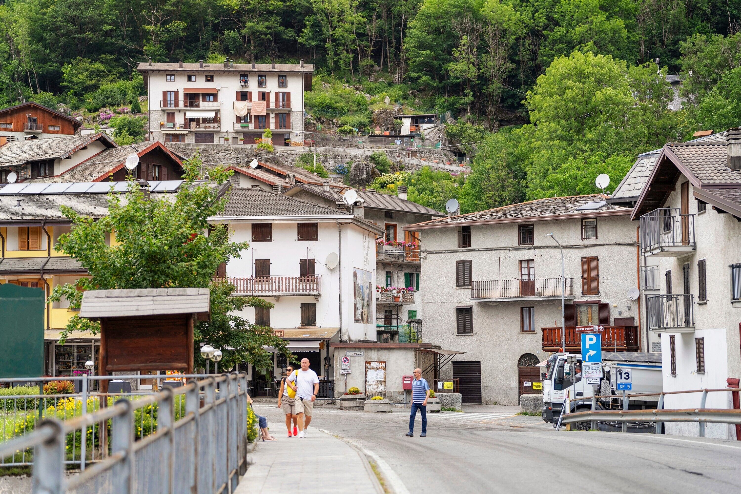Una strada residenziale con case, un camion parcheggiato e un attraversamento pedonale.