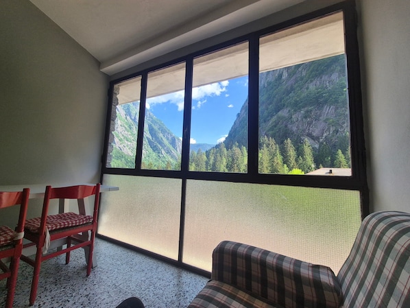 A room with a large window, a red chair, a plaid sofa, and a textured floor.
