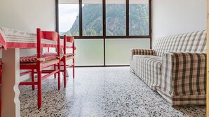 Ein Zimmer mit Esstisch, Stühlen, einer Couch und einem großen Fenster mit Blick auf die Berge.