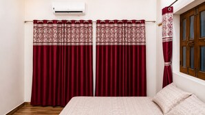 Un dormitorio con cama, dos cortinas rojas con un borde estampado, suelo de madera y una ventana con marco de madera.
