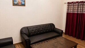 Un sofá de cuero negro, una mesa de centro de madera y una cortina roja en una habitación con pared lisa y un cuadro enmarcado.