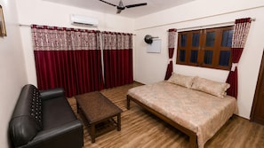 A bedroom with a bed, a sofa, a small table, and a ceiling fan. - Balaji Hotel (Farrukhabad)