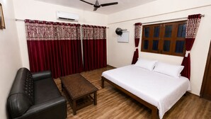 Una habitación con una cama, un sofá de cuero negro, una mesa de madera y cortinas rojas.
