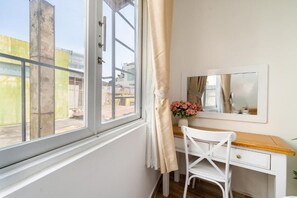Quarto com escrivaninha branca, uma cadeira, janela com cortina e espelho na parede.