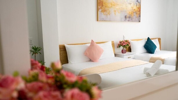 Quarto de hotel com uma cama, mesa de cabeceira, um vaso com flores e um quadro na parede.
