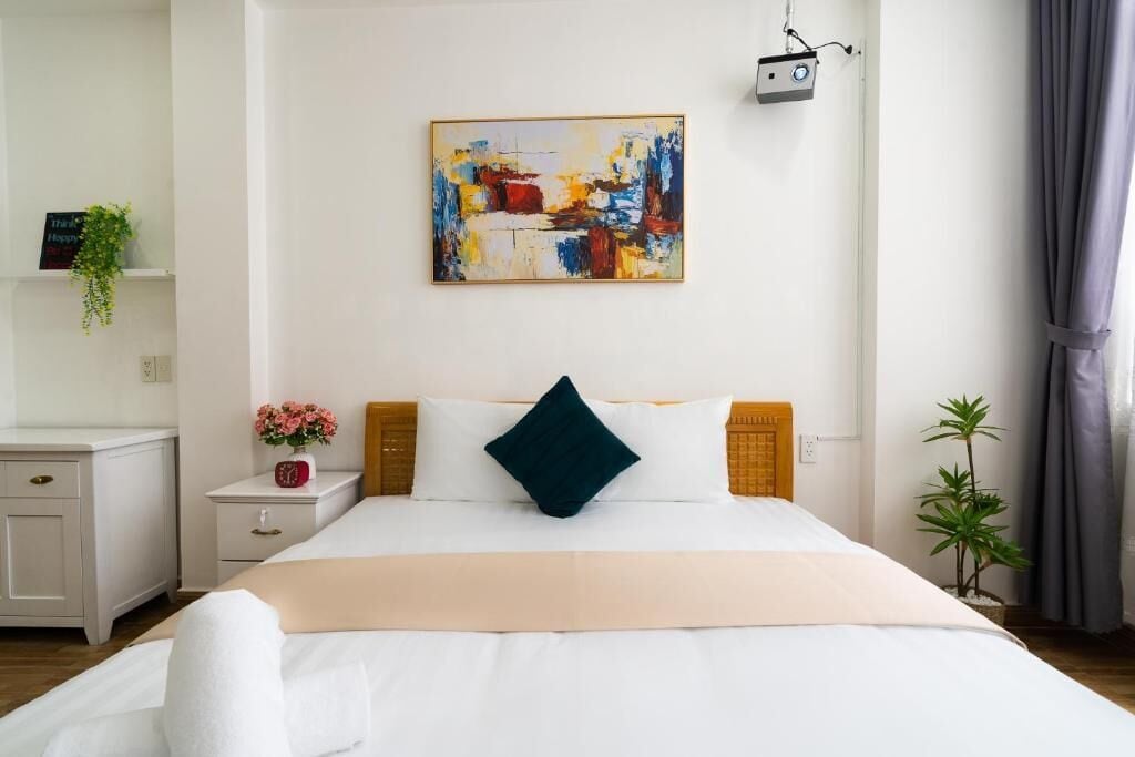 Habitación de hotel con una cama, una mesita de noche, un televisor montado en la pared y un cuadro.
