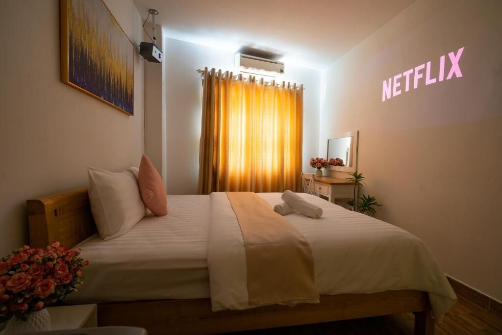 Une chambre d’hôtel comprenant un lit, une table de chevet, un miroir, un climatiseur fixé au mur et un rideau.