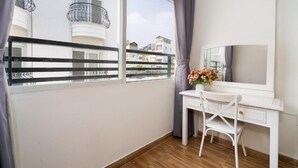 Quarto com escrivaninha, cadeira e uma janela grande com vista para uma varanda.