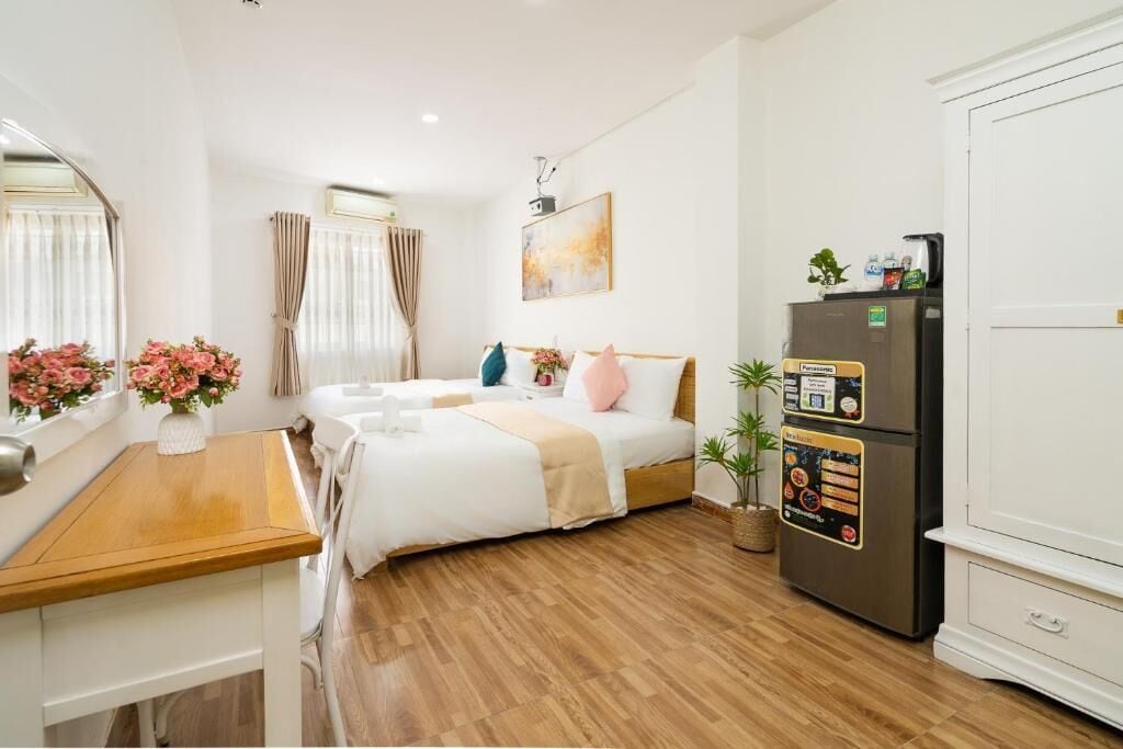A hotel room with a bed, a wooden desk, a refrigerator, and a window with curtains.