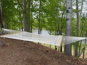 A hammock between trees in a forested area with a body of water in the background.