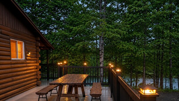 Une terrasse en bois avec une table de pique-nique et des bancs, entourée d’une clôture en bois et d’arbres.