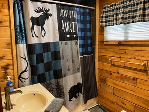 A bathroom with a checkered shower curtain, a sink, and wooden walls. - Hambrook Point Cottage | Renous & Miramichi Rivers (Renous)