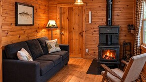 L’intérieur chaleureux d’un chalet avec un canapé, un fauteuil à bascule, un poêle à bois et une illustration encadrée représentant un poisson accrochée au mur.