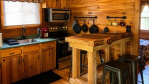 Une cuisine rustique, située dans une cabane en bois, équipée d’un four à micro-ondes, d’une cuisinière et de casseroles suspendues.