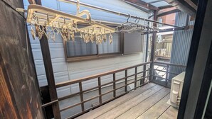 A wooden deck with a metal railing, a clothesline, and a window with blinds. - NAKAZAWA Home (Osaka)