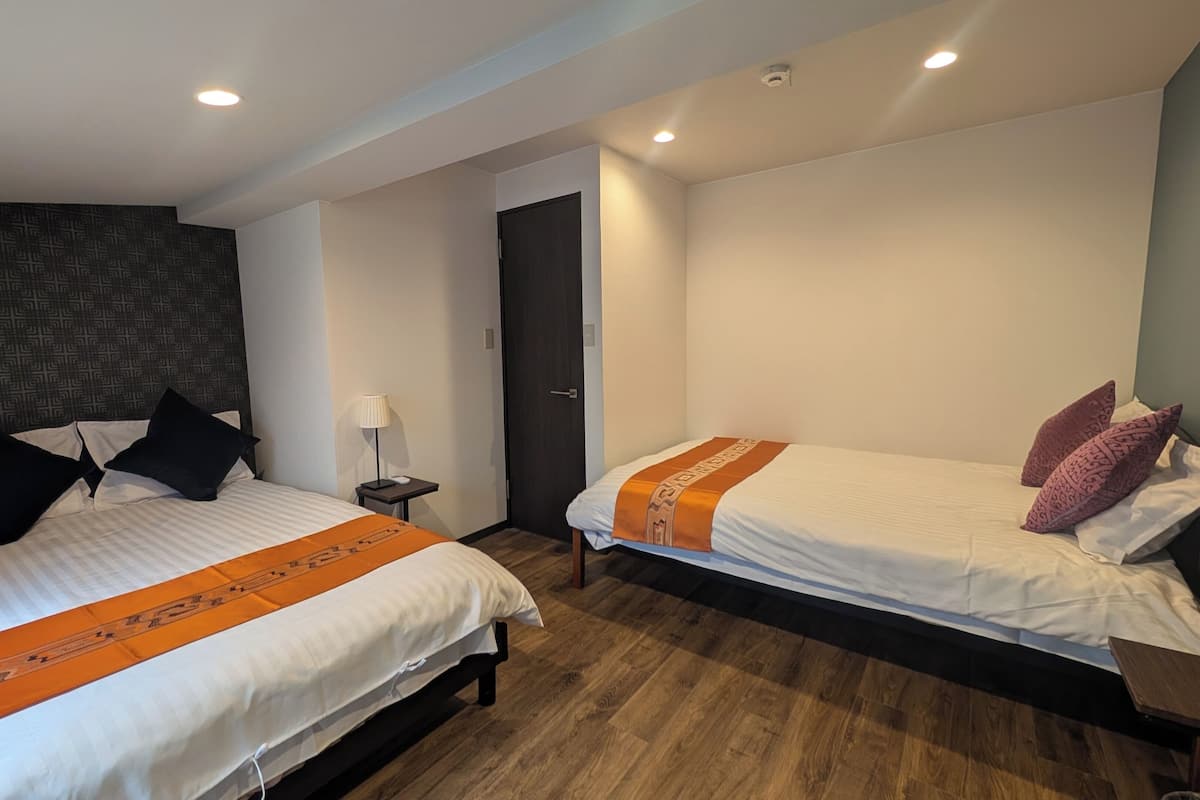 A hotel room with two beds, a dark patterned headboard, a wooden floor, and a door.
