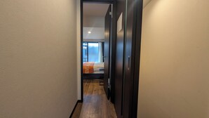 A narrow hallway with a wooden floor leading to a bedroom with a bed and a window. - NAKAZAWA Home (Osaka)