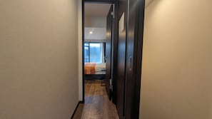 Ein schmaler Flur mit Holzboden führt zu einem Schlafzimmer mit Bett und Fenster.