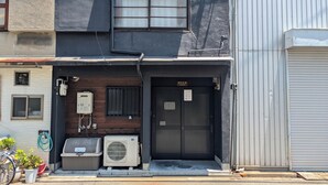 A building with a black door, a window with bars, and an air conditioning unit on the ground floor. - NAKAZAWA Home (Osaka)