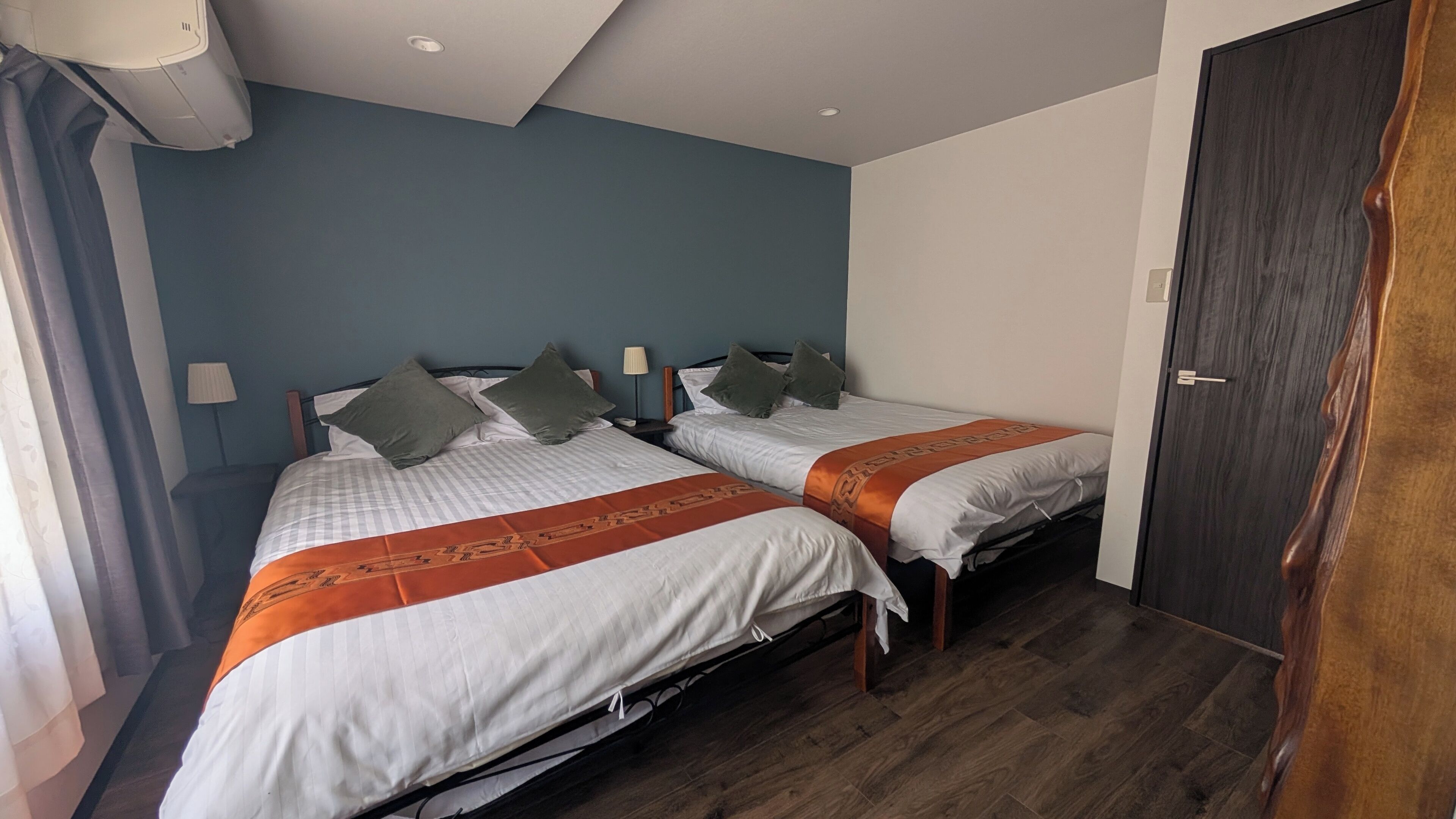 A hotel room with two beds, a dark wooden door, and a blue accent wall.