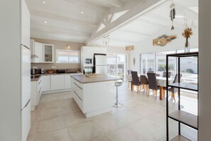 A modern kitchen with white cabinetry, a central island, and a dining area with a view. - Villa Tikaz 4* Ile d'Oléron 8 people swimming pool (Saint-Denis-d'Oléron)