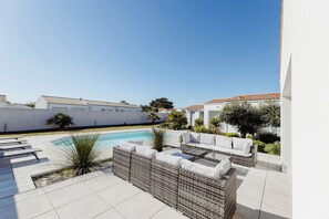 A modern outdoor patio with a pool, wicker furniture, and a white wall.