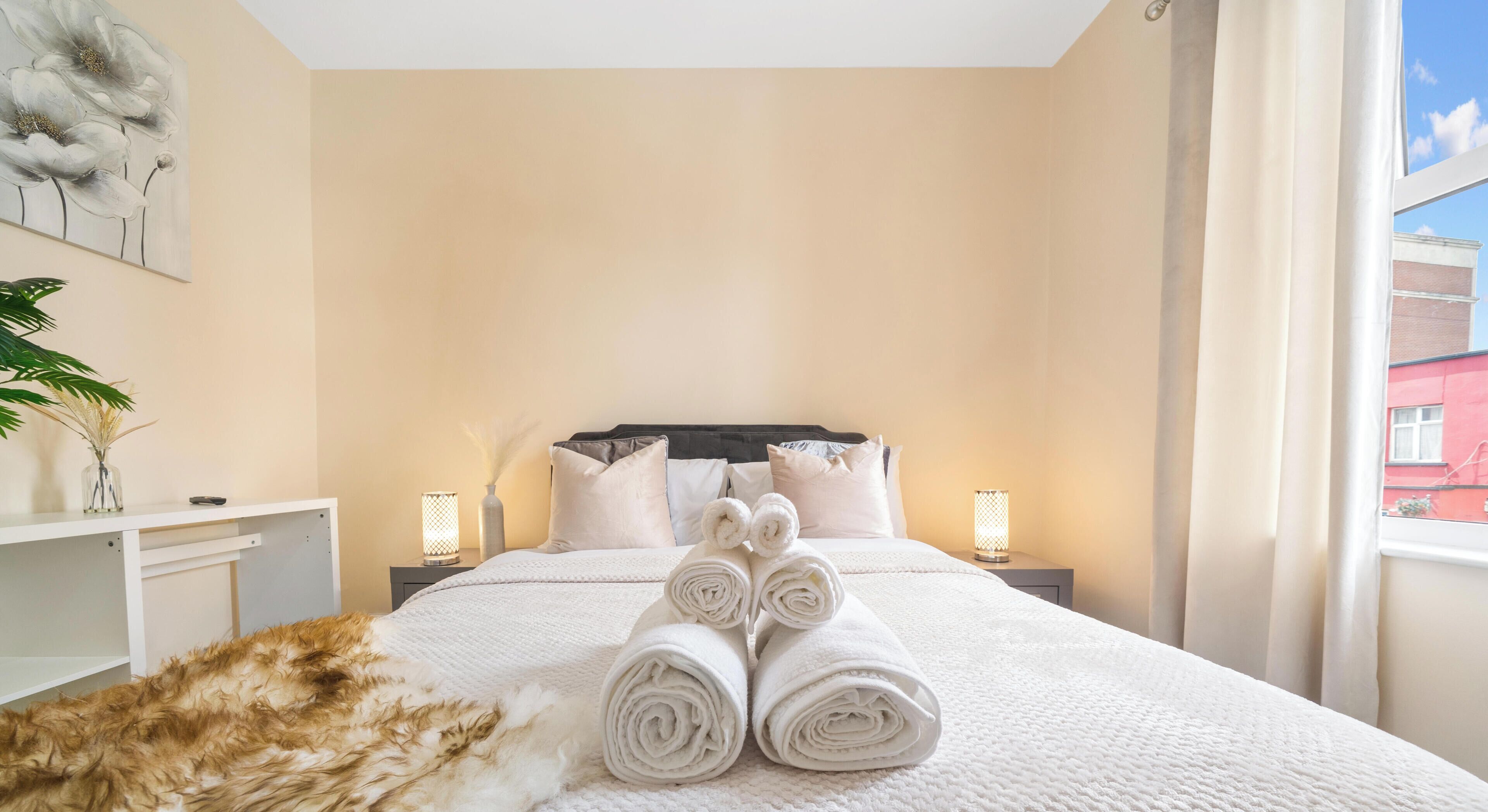 Habitación de hotel con una cama, almohadas, una mesita de noche con lámpara, un escritorio y una ventana con cortinas.