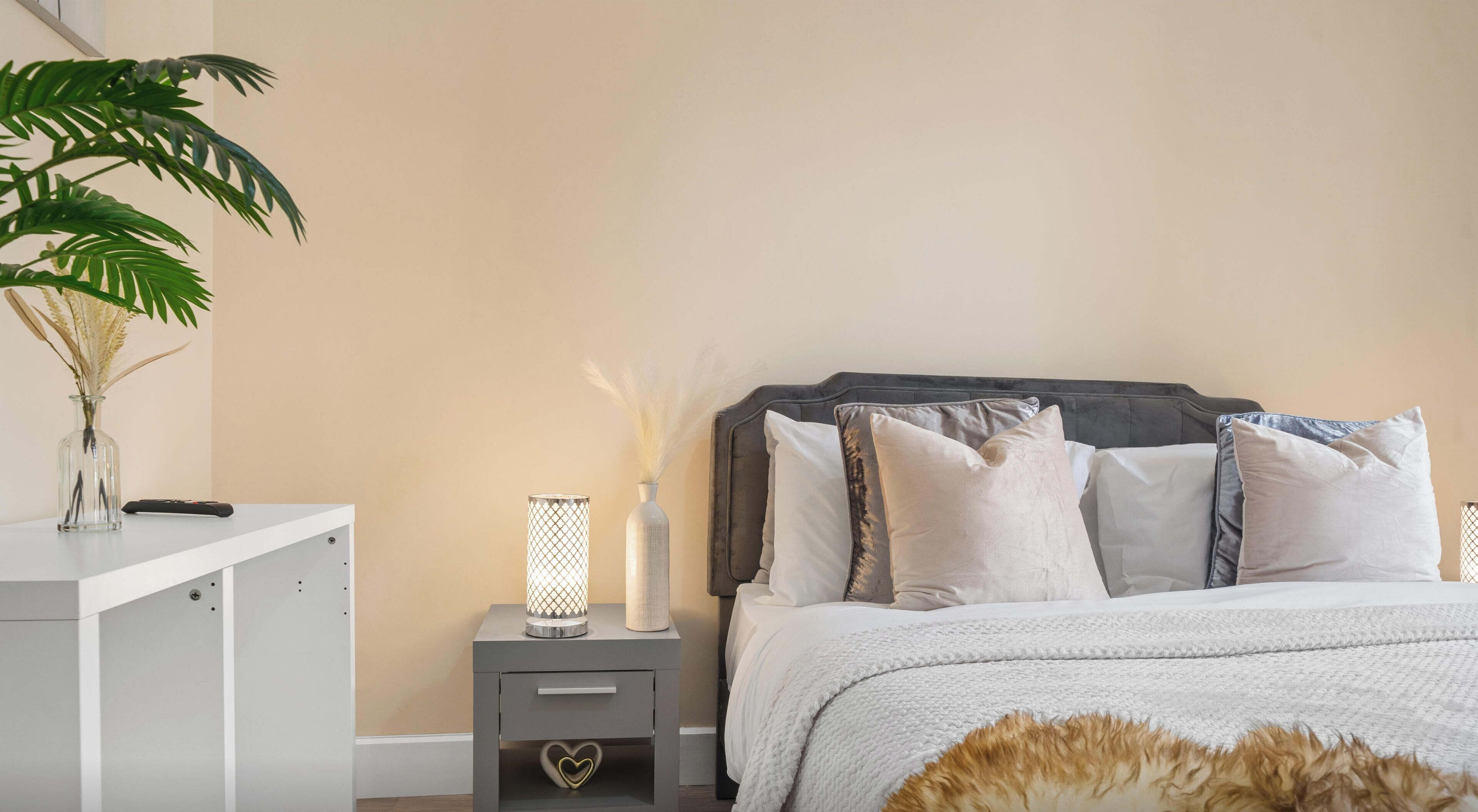 Une chambre à coucher comprenant un lit, des tables de chevet, une commode, une lampe, un vase contenant des plantes séchées et une plante en pot.